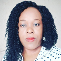 A woman with curly black hair wearing pearl earrings and a white blouse with black polka dots looks directly at the camera against a light-colored background.
